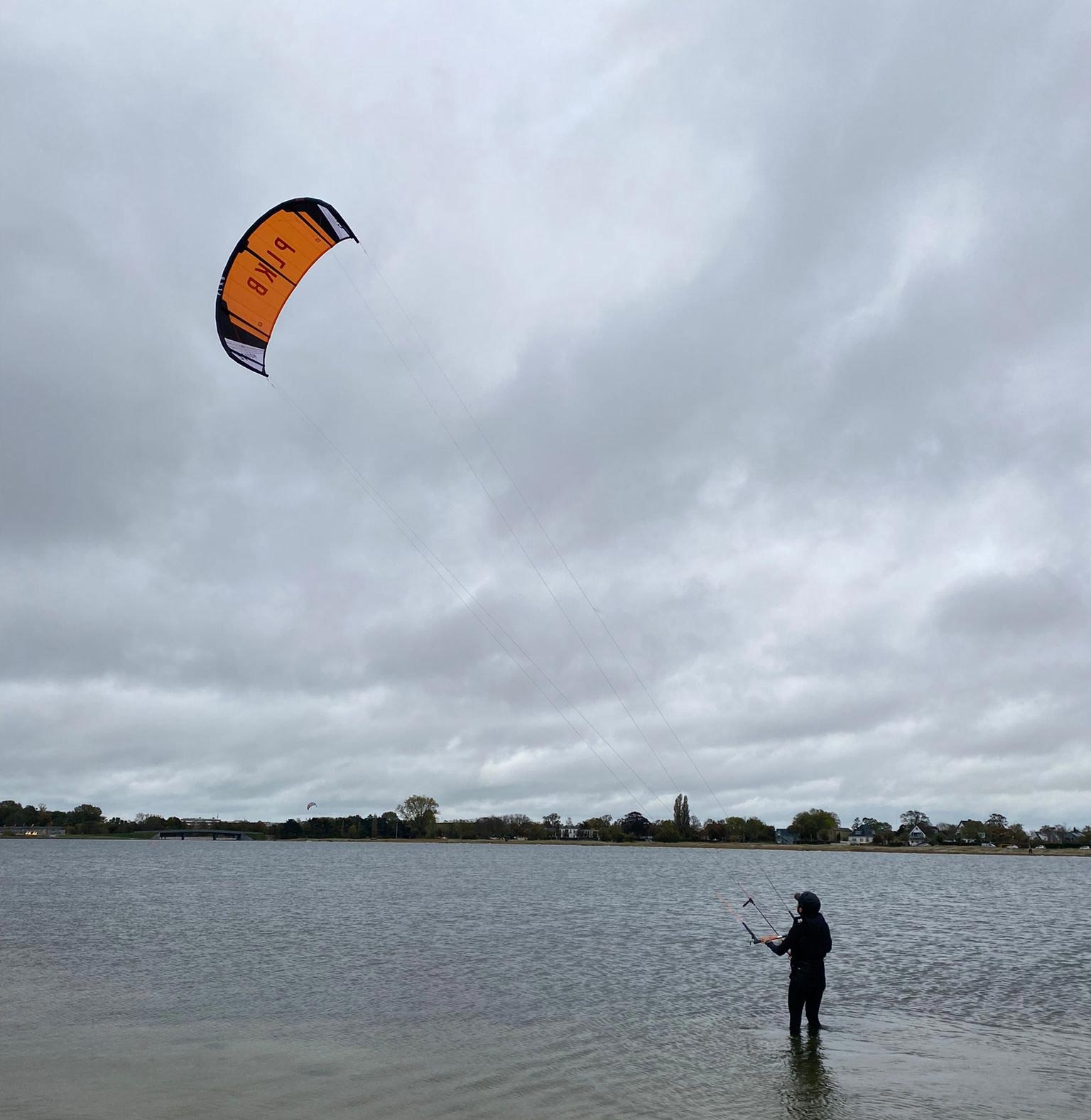 man with a kite in water with grey sky